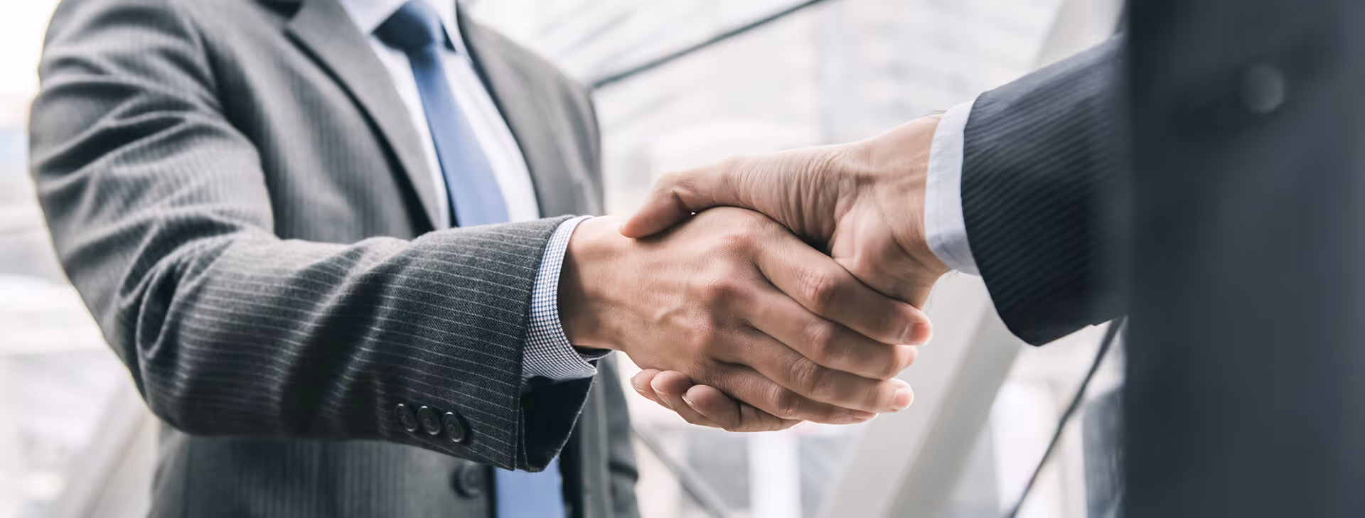 Close-up of two businesspeople in suits shaking hands in an office setting.