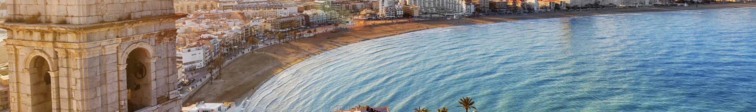 Photo of a Spanish coastal destination with the beach, sea, buildings along the coastline on a sunny day. 