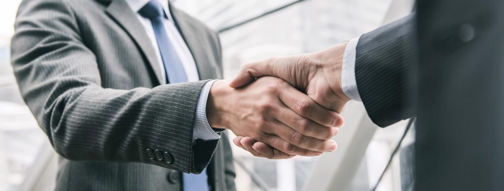 Two people in suits, most likely business people shaking hands. 