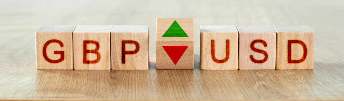 Building blocks with letters that spell out GBP and USD. One building block in the middle has both a green and red arrow pointing up and down. 