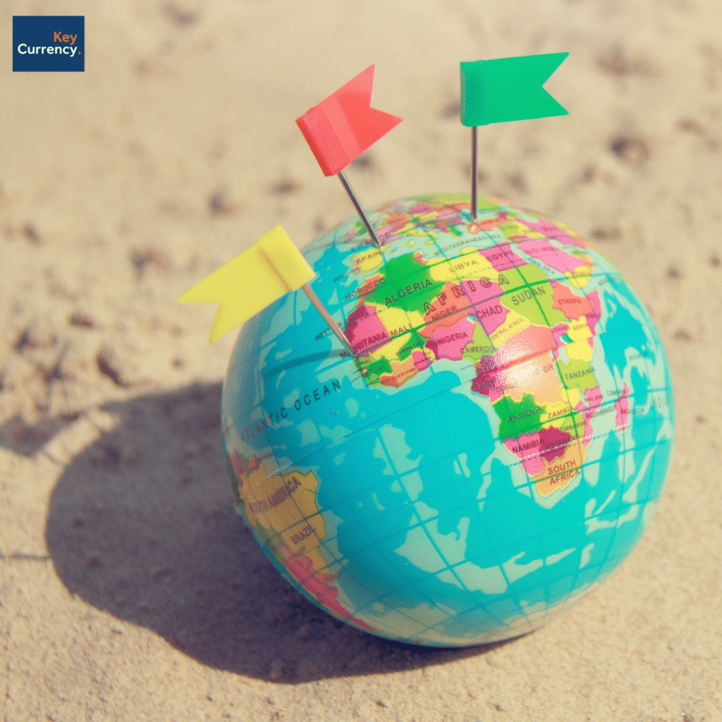 Small globe of the world with flags planted in various destinations. Placed on a beach.