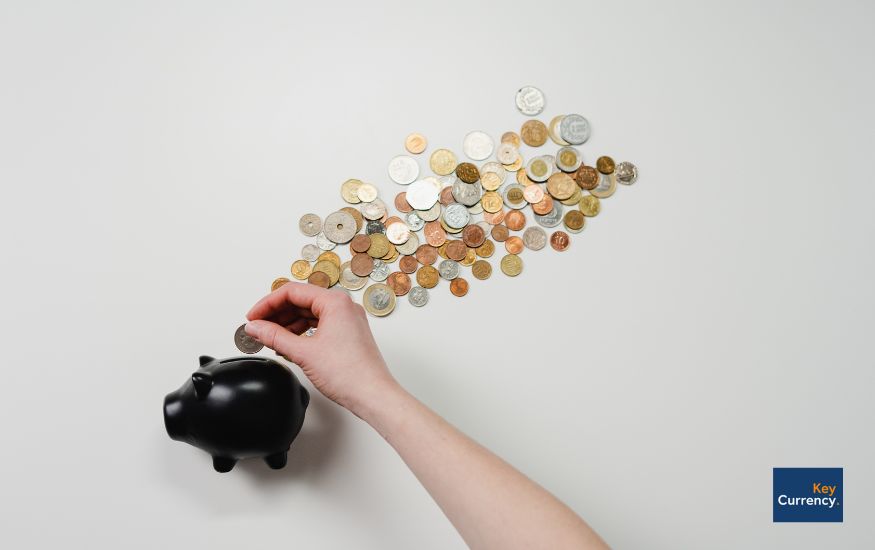 Hand of a person putting in coins into a black piggy bank infront of a white background. 