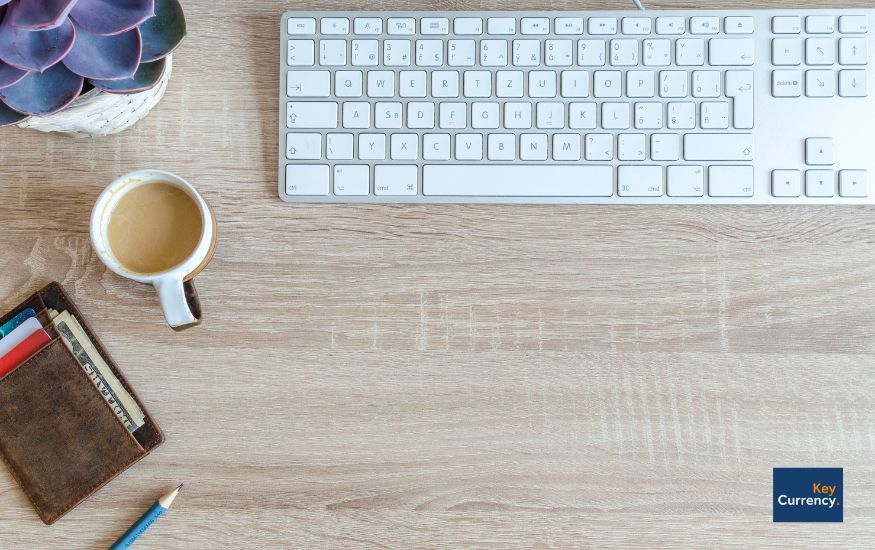 Overhead photo of an office desk including a keyboard, potted plant, cup of tea, wallet and a pen. 