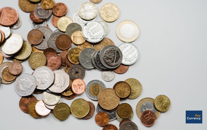 Various different currency coins scattered across a grey background. 