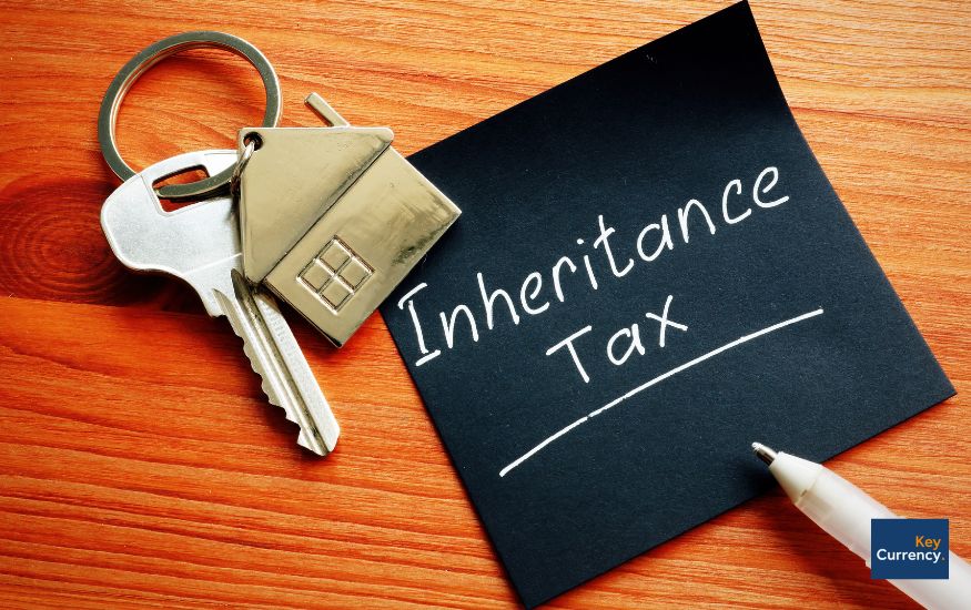 A black post-it note with 'inheritance tax' written on it. This note is placed next to a silver key with a house key ring attached to it. 