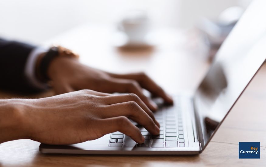 Close up of a person's hands typing on a laptop in what looks like an office setting or at a home office. 