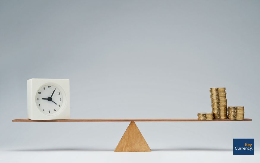 A wooden scale with coins on one side and a timer on the other. Representing that timing is important when making a foreign exchange transfer.