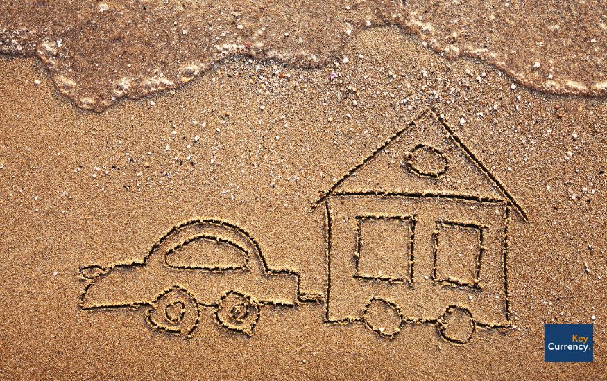 A drawing in sand of a car pulling along a house with wheels.