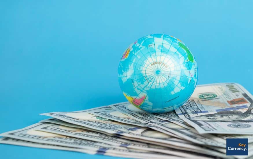 a blue background with scattered currency bills and a globe of the earth resting on top to depict international money transfers.